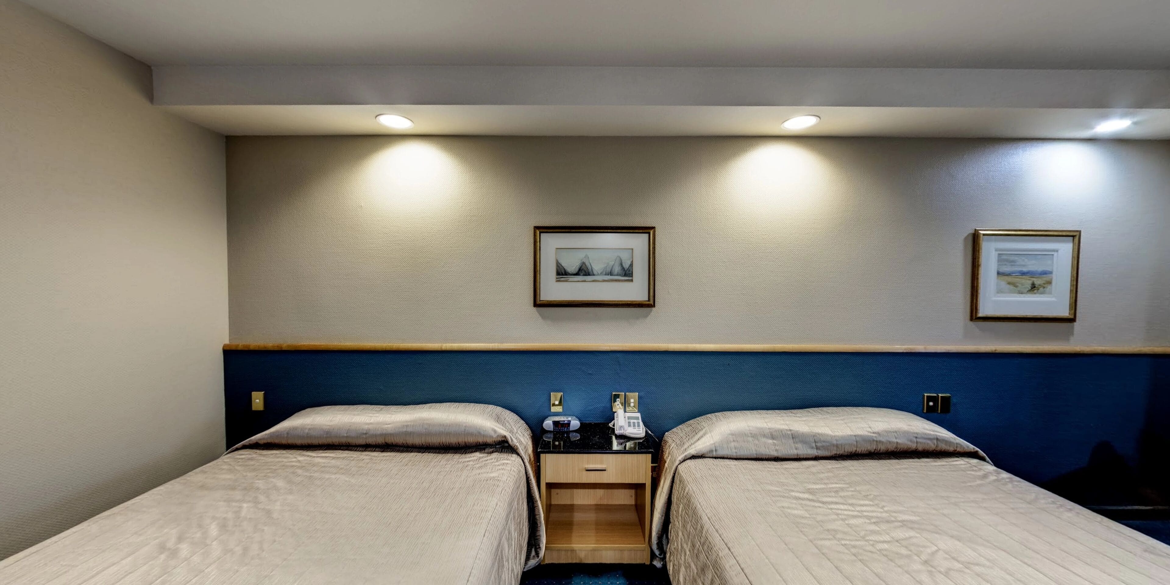 A hotel room with two beds, a nightstand, a phone, and two framed pictures on the wall.