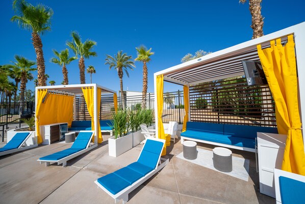 A rooftop pool area with sun loungers, yellow curtains, and palm trees. - The Nautical Beachfront Resort (Lake Havasu City)