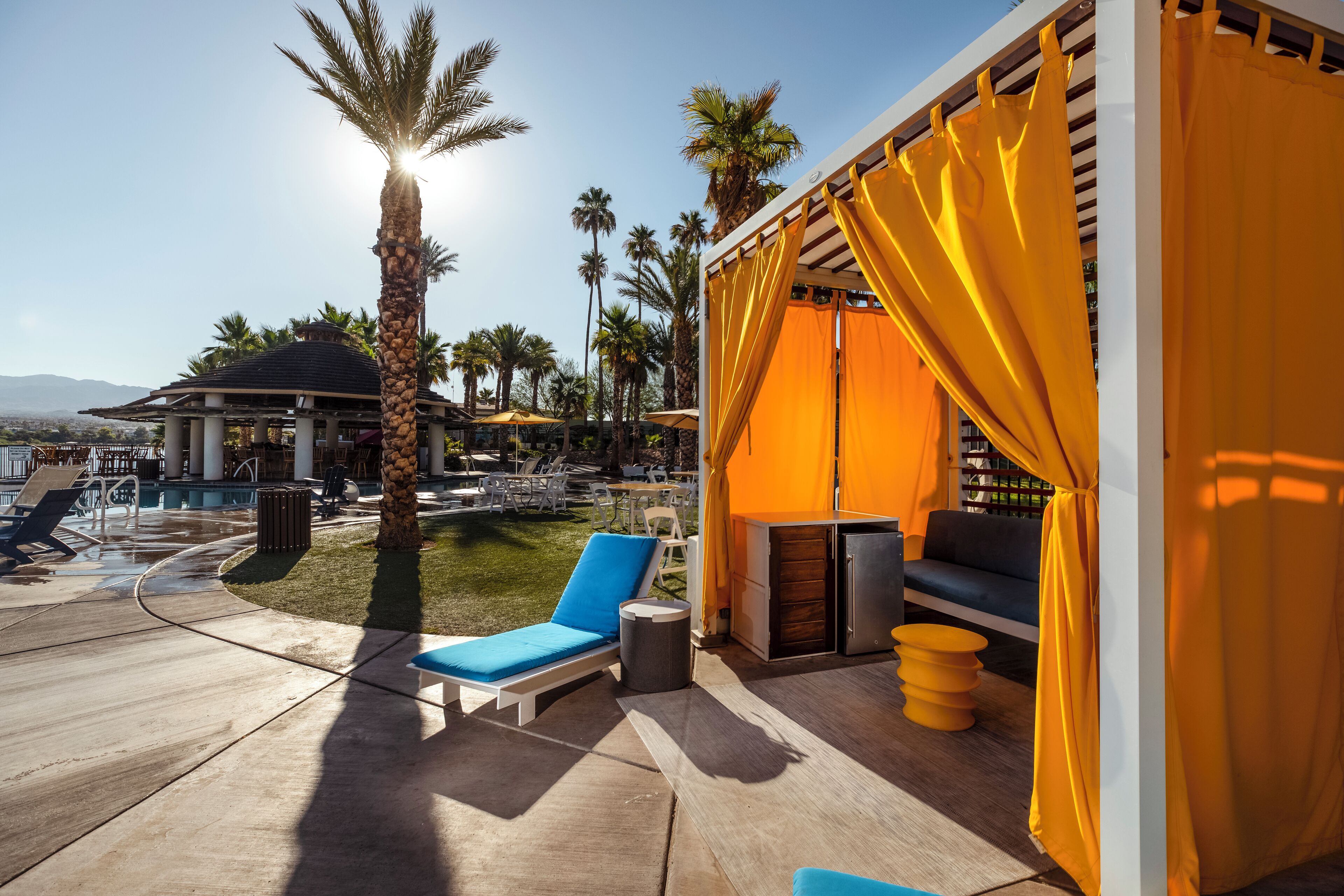 A poolside area with lounge chairs, a small table, and a covered seating area with yellow curtains.
