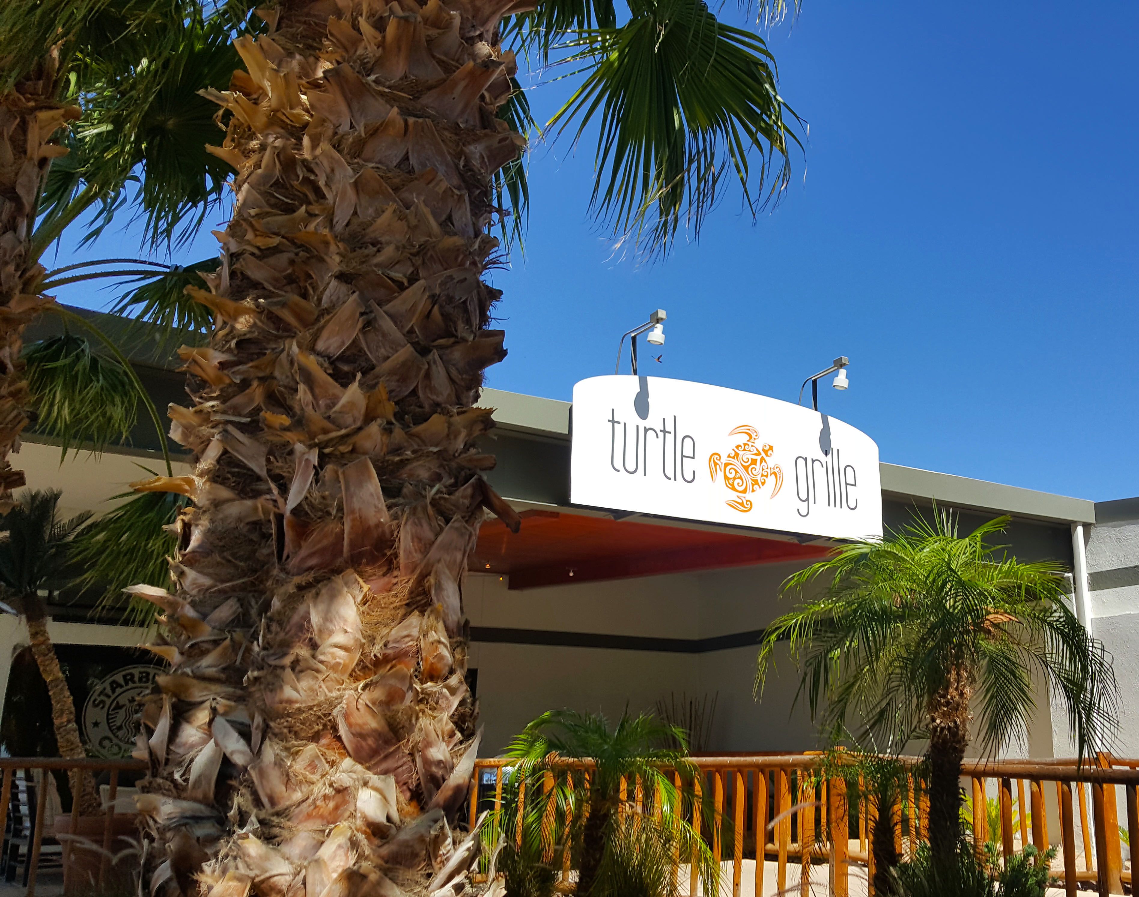 A sign for 'turtle grille' with a modern building in the background.