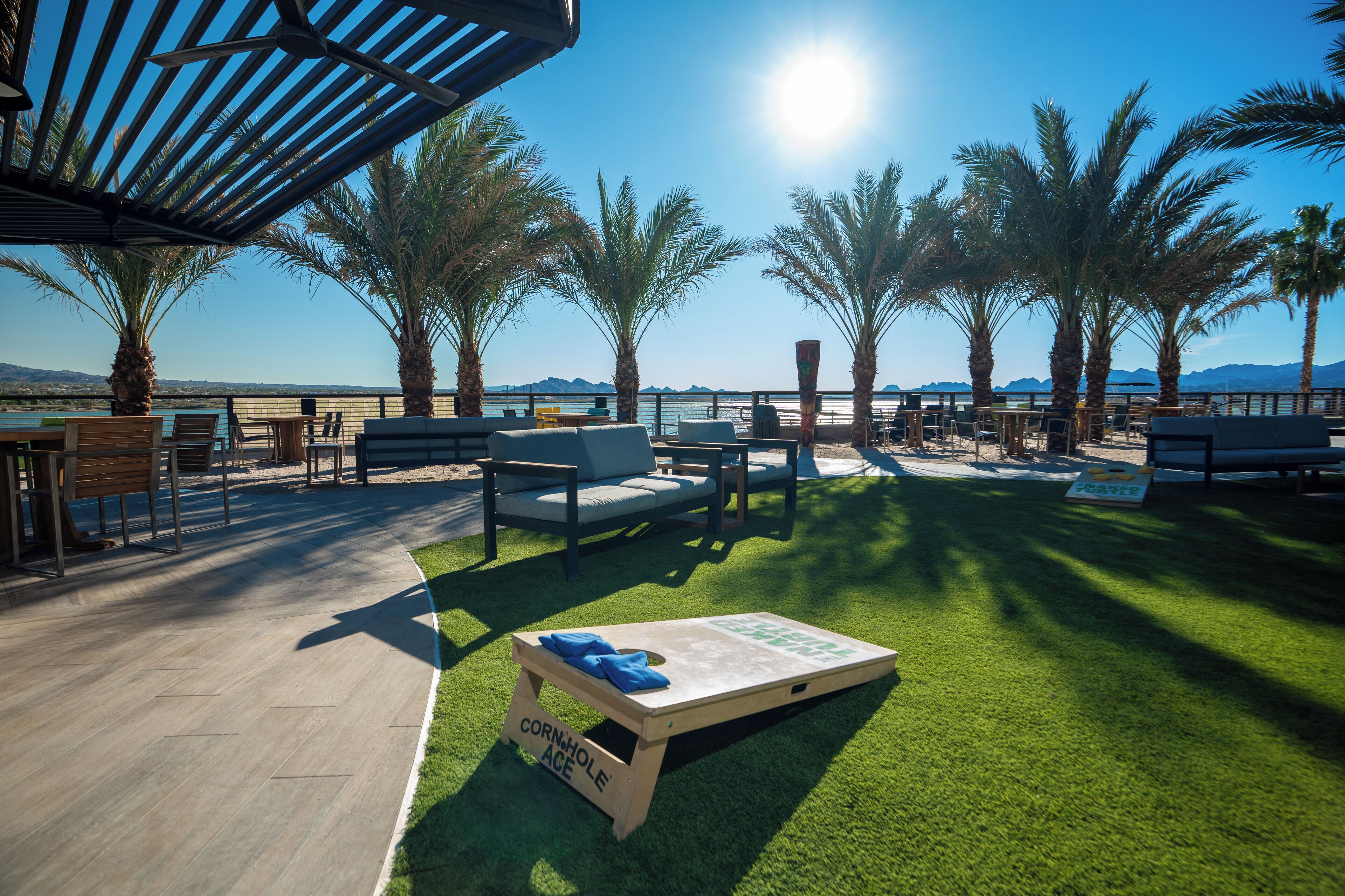 A terrace with outdoor seating, a corn hole game, and a view of the sea and mountains.