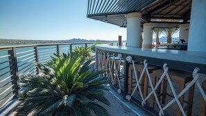 Een balkon aan zee met uitzicht op de oceaan en bergen, met een houten leuning en een rieten dak.