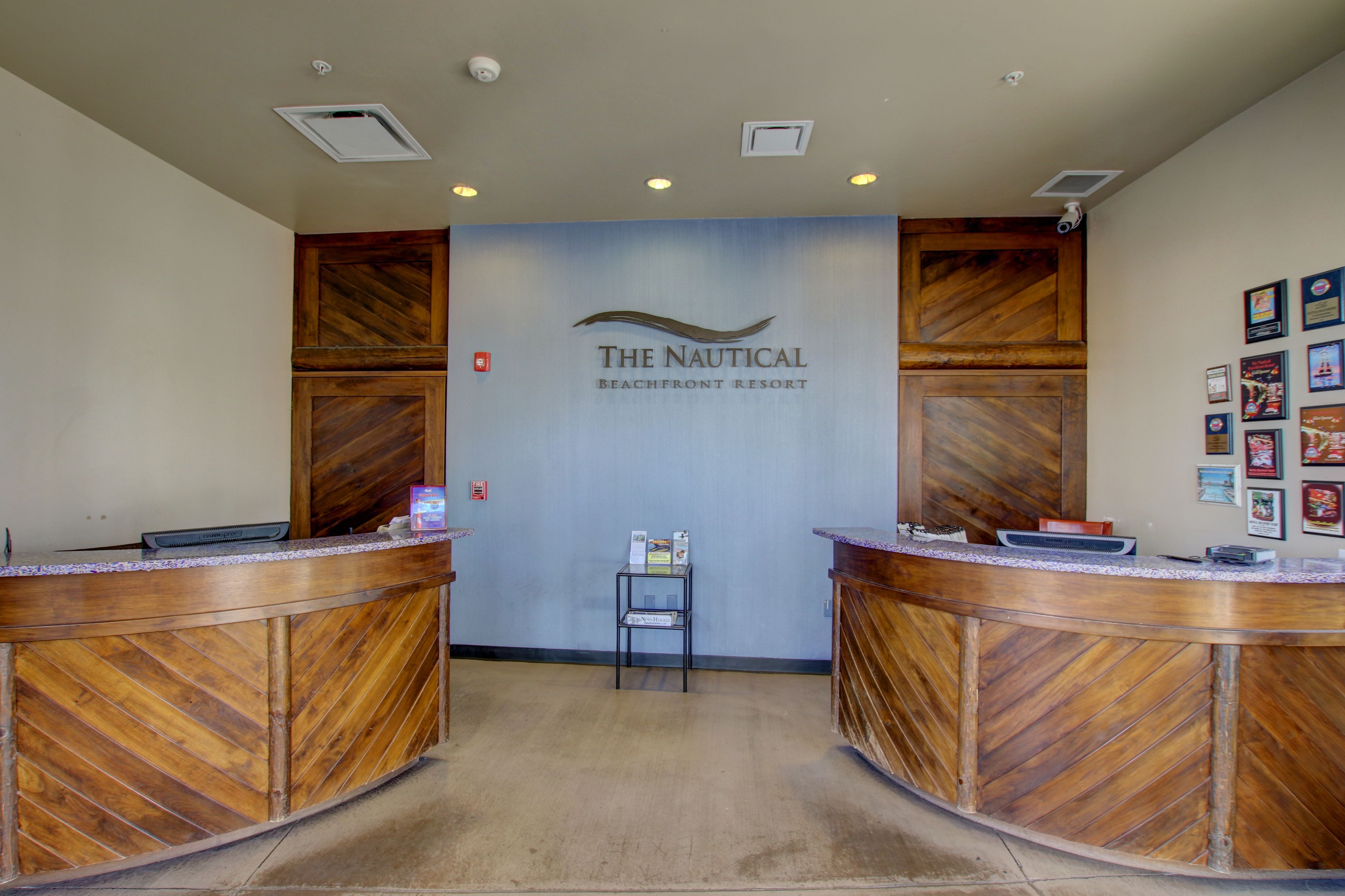 A reception area with two wooden reception desks, a wall-mounted sign reading "The Nautical Beachfront Resort", and a small chair in front.