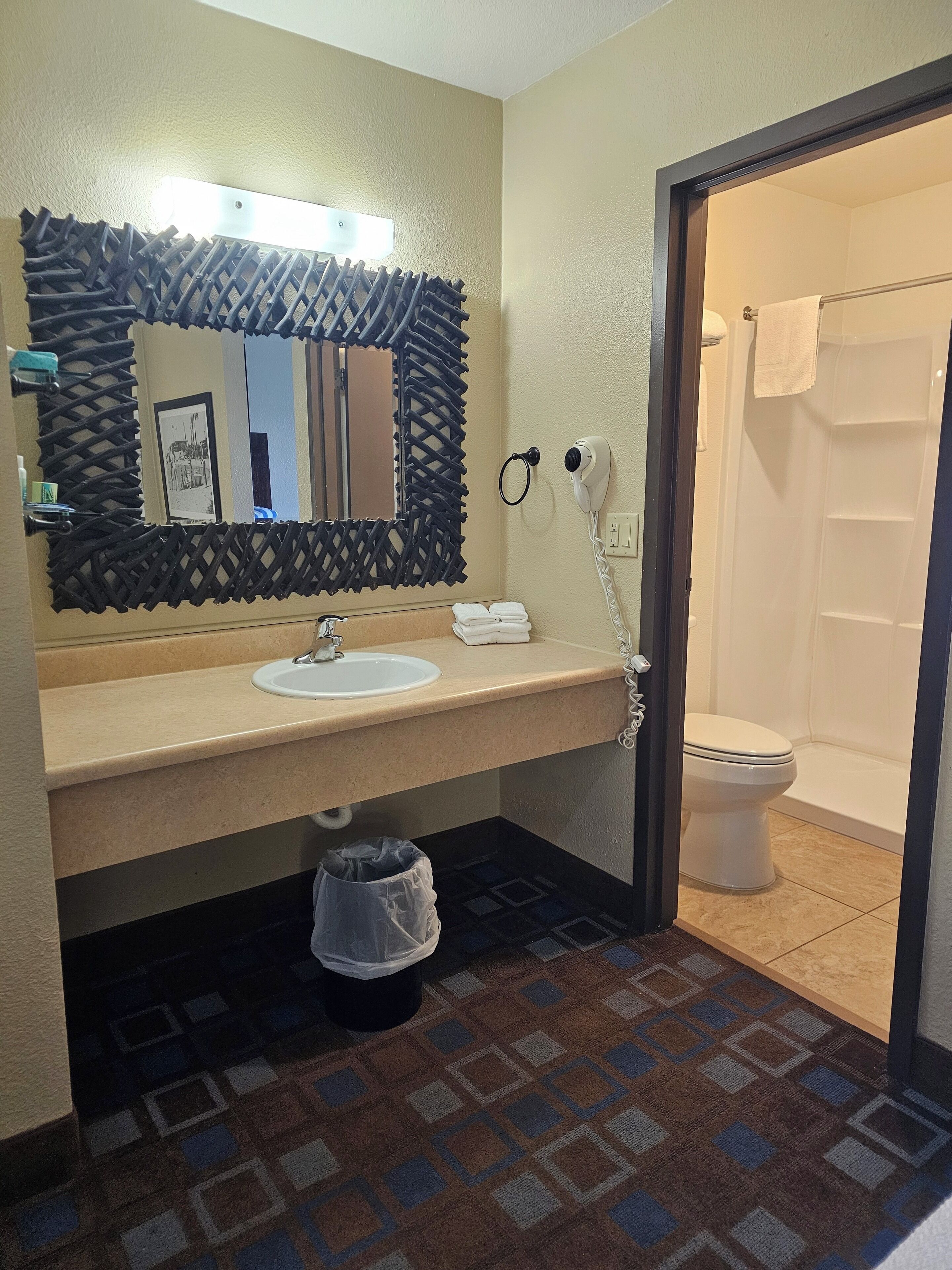 Un baño con lavamanos, espejo y retrete. Incluye un perchero, secador de pelo y cubo de basura.