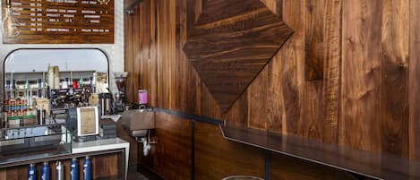 A coffee shop interior with a wooden wall, a menu board, and a counter with stools.