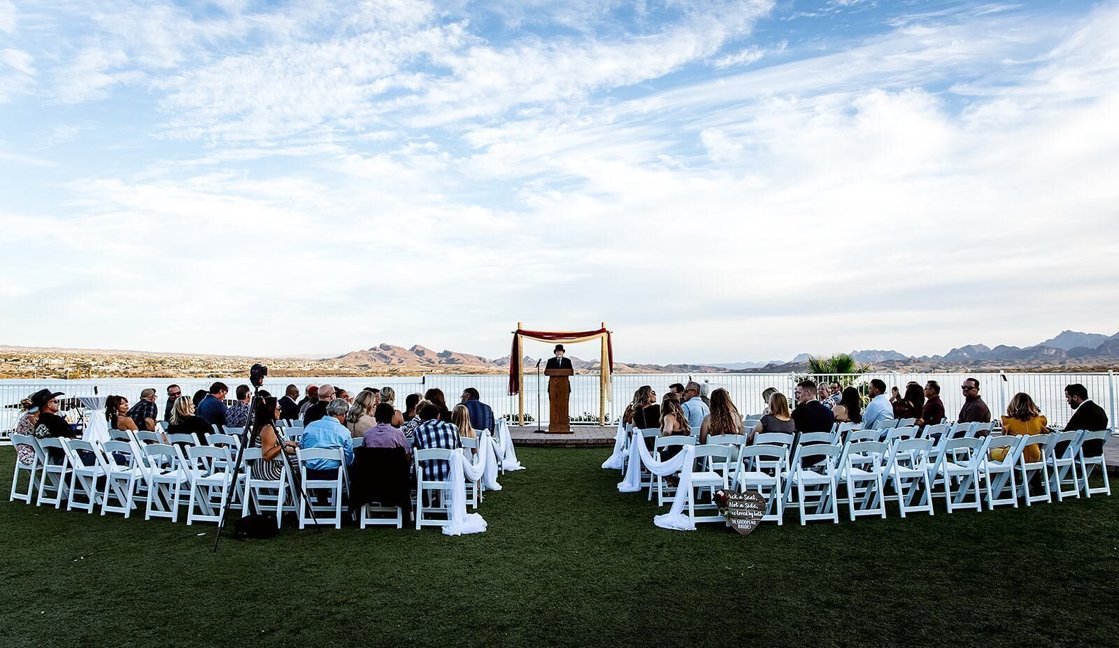 An outdoor wedding ceremony with guests seated in rows facing a wooden arch.