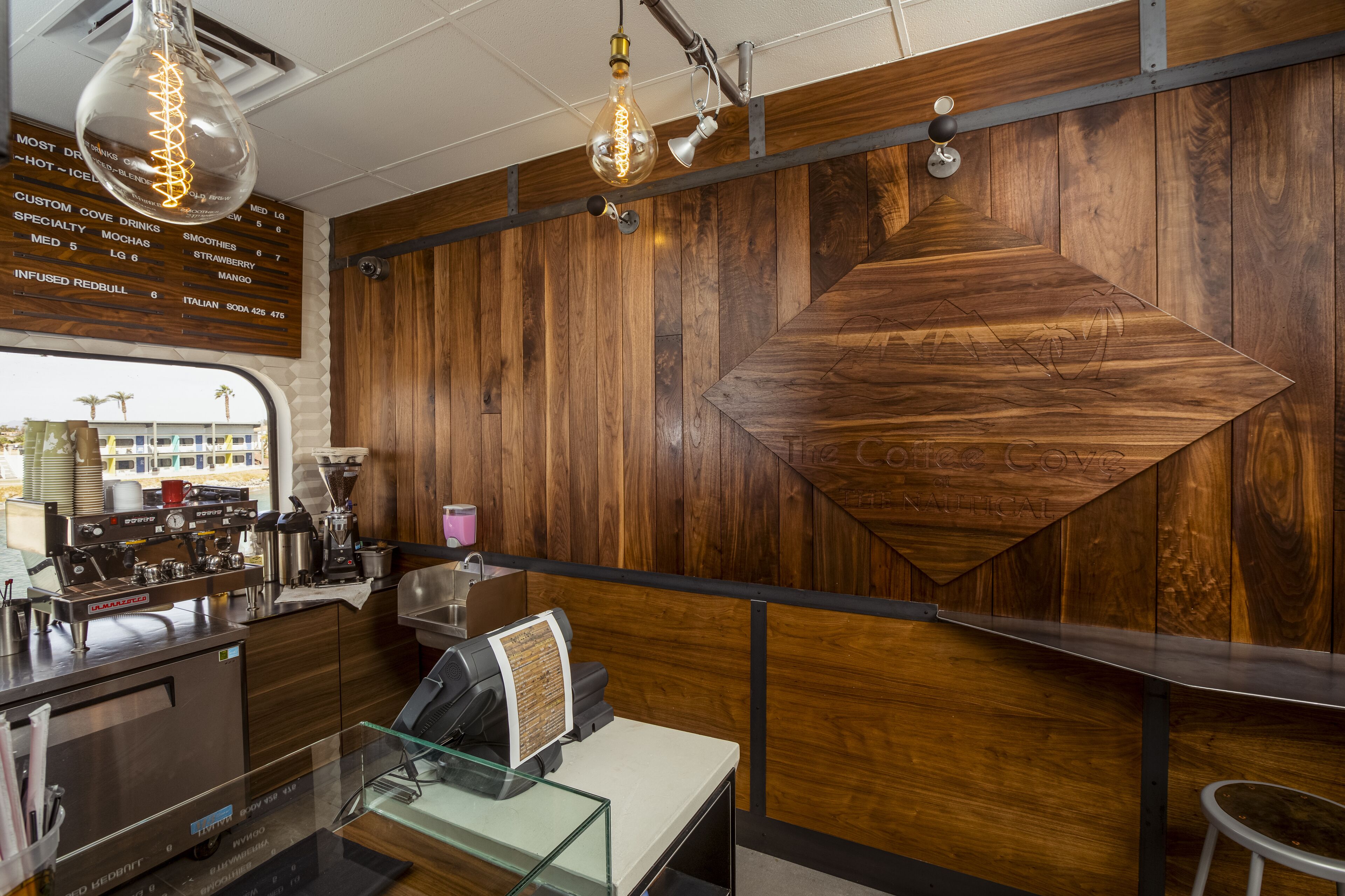 A coffee shop interior with wooden paneling, a menu board, espresso machines, and a glass display case.