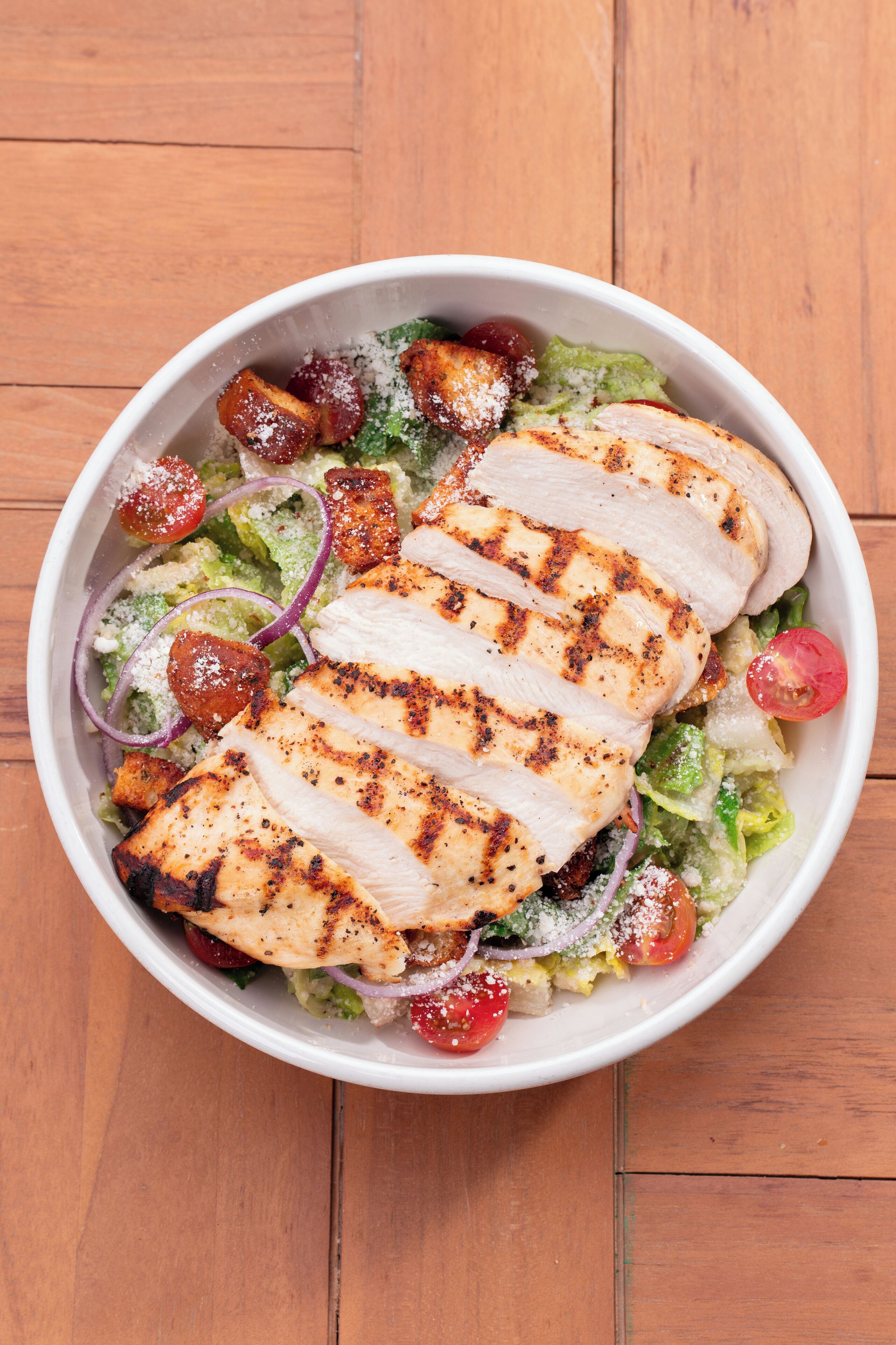 A bowl of salad with grilled chicken, tomatoes, and red onions.