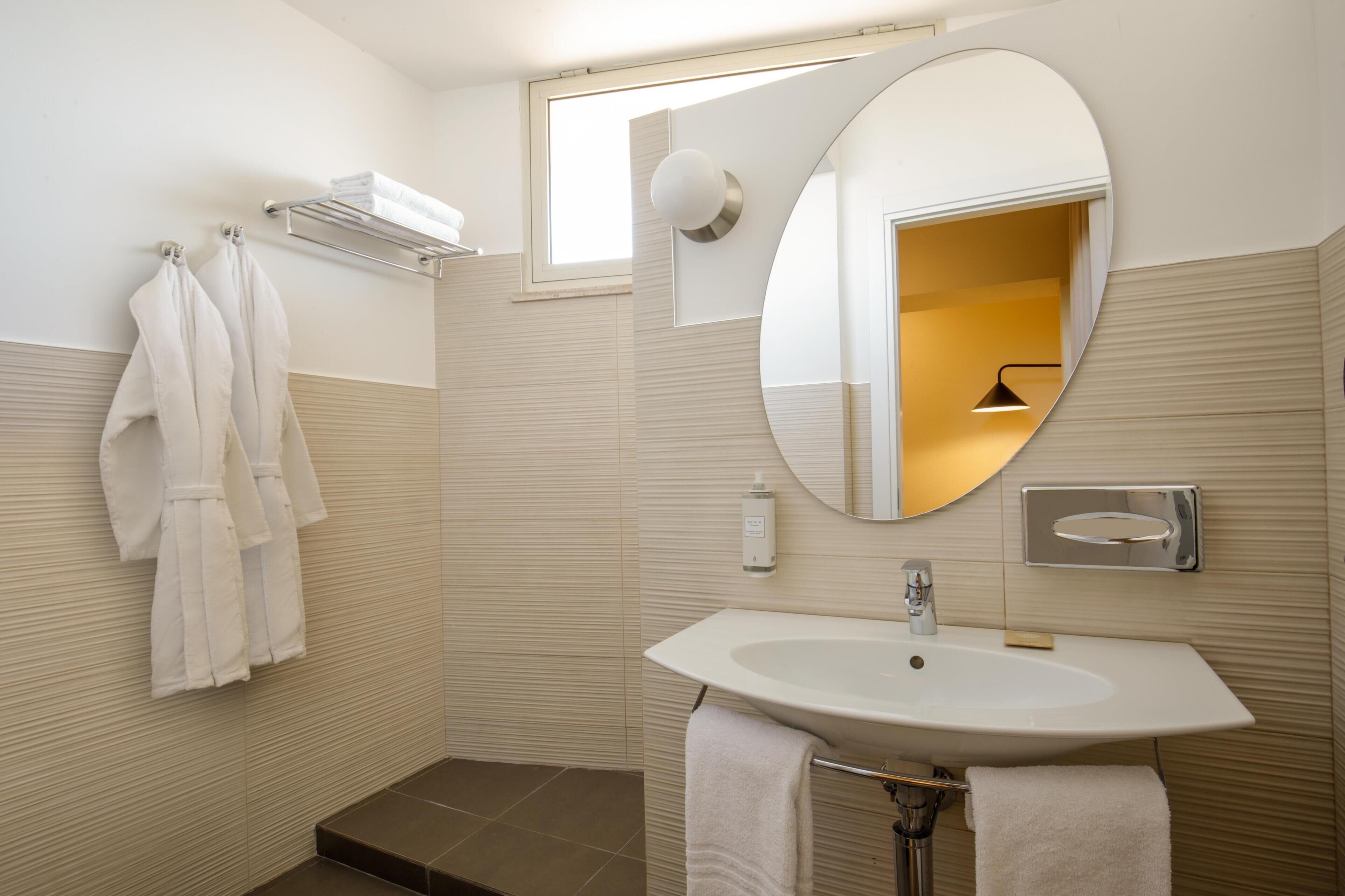 A modern bathroom with a large oval mirror, a white sink, and two towels hanging on the wall.