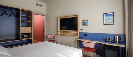 A hotel room with a bed, a desk, a chair, a wardrobe, a TV, and a small refrigerator.