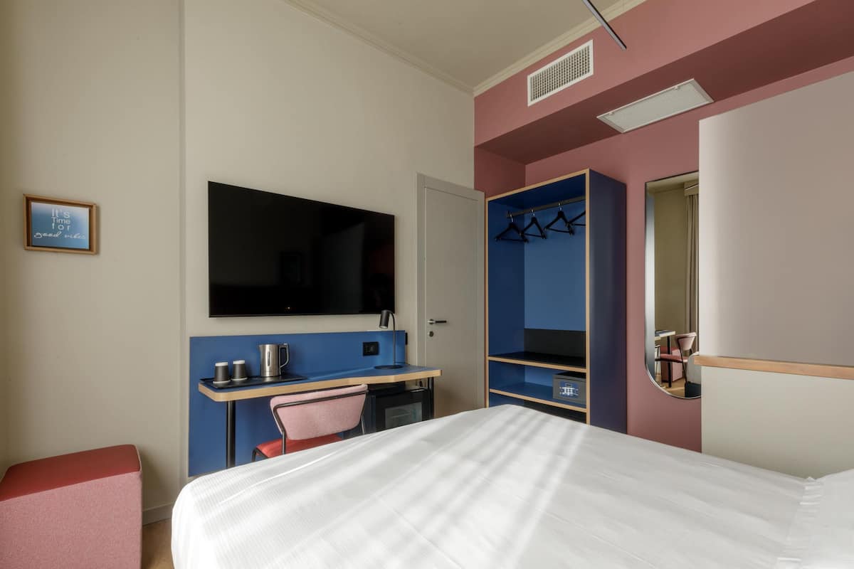 Hotellihuone, jossa on sänky, työpöytä, tuoli, televisio, vaatekaappi ja peili.