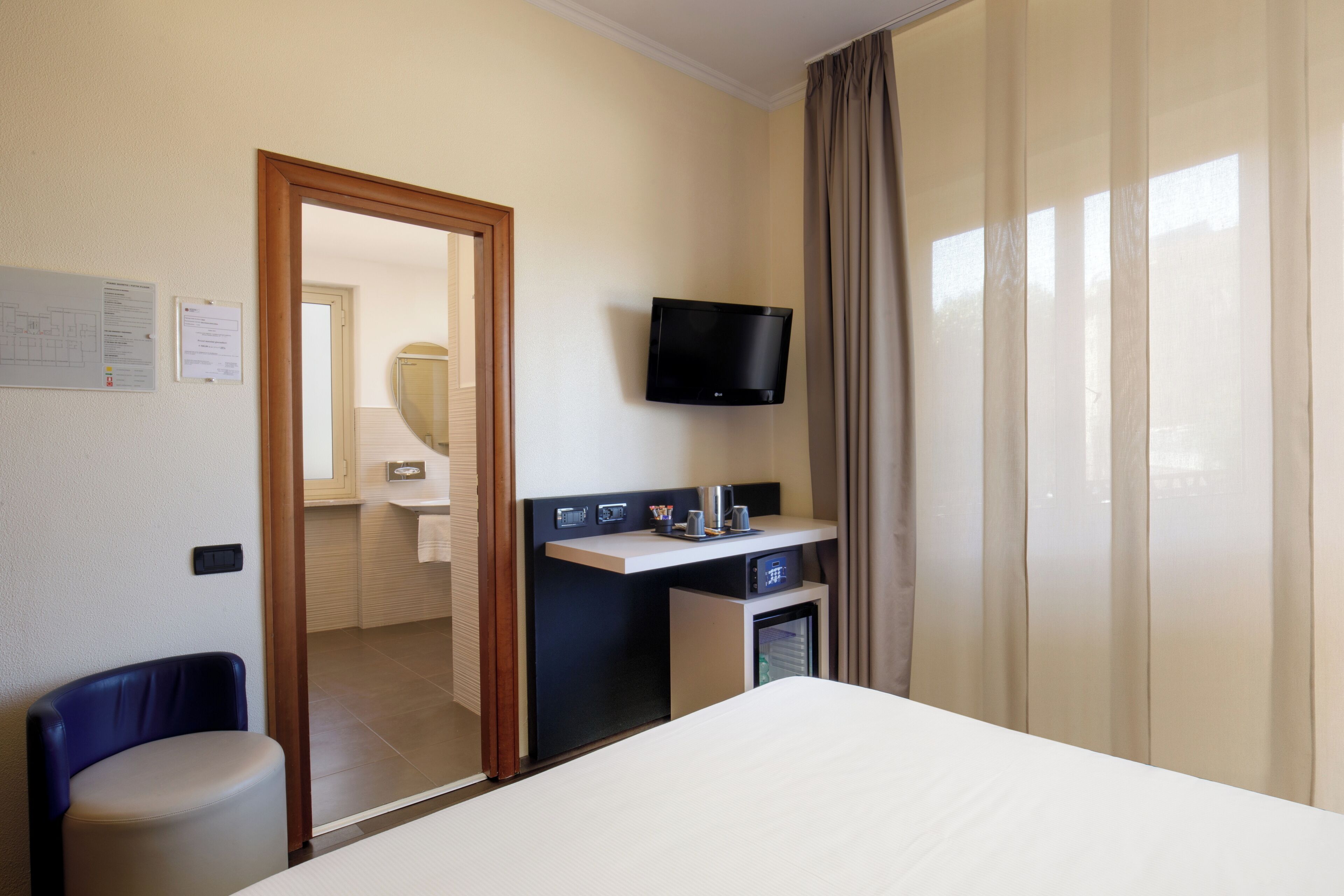 A hotel room with a bed, a desk with a television, a chair, and a small refrigerator.