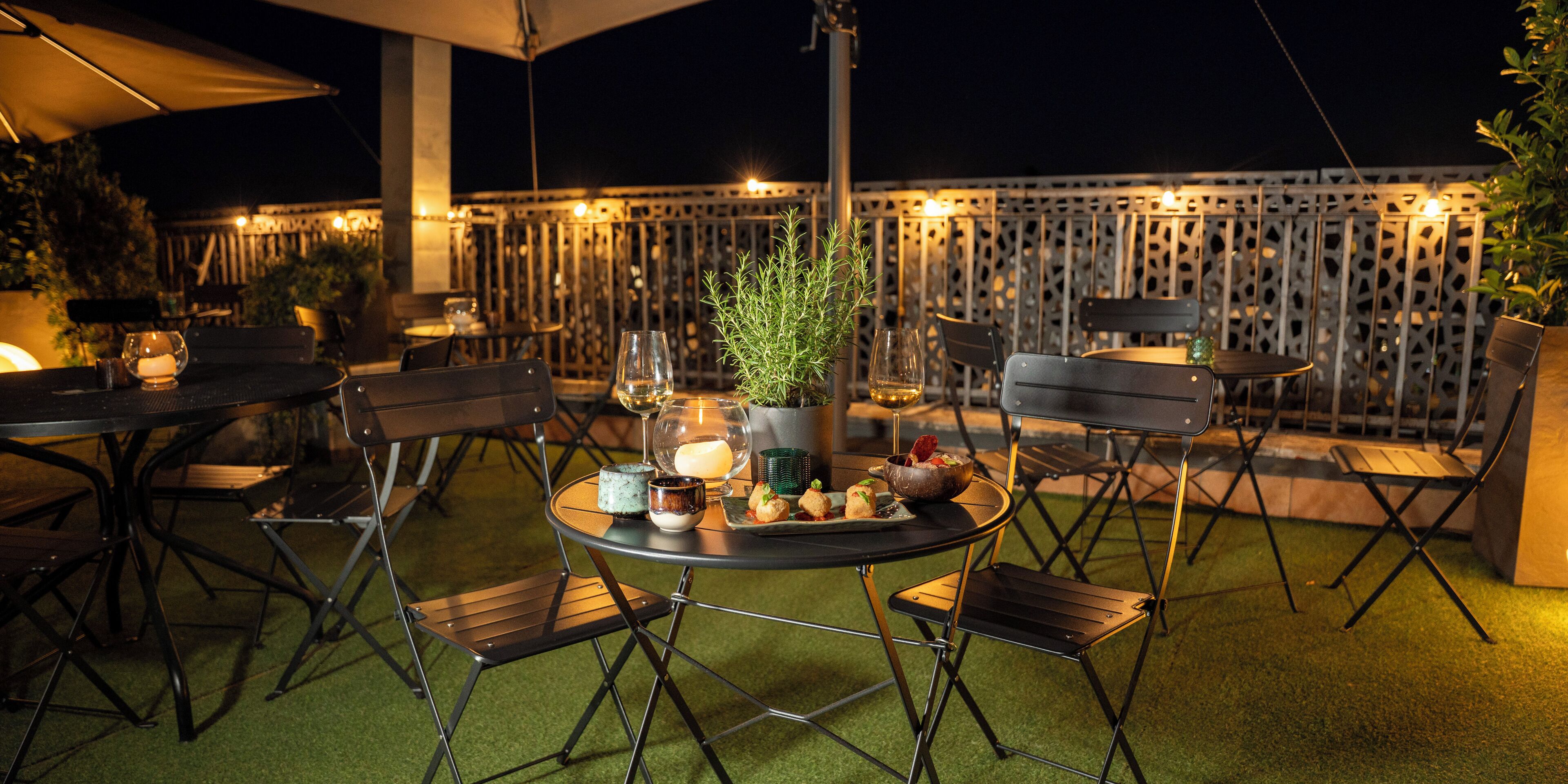 An outdoor dining area with tables and chairs, a potted plant, and a decorative fence.
