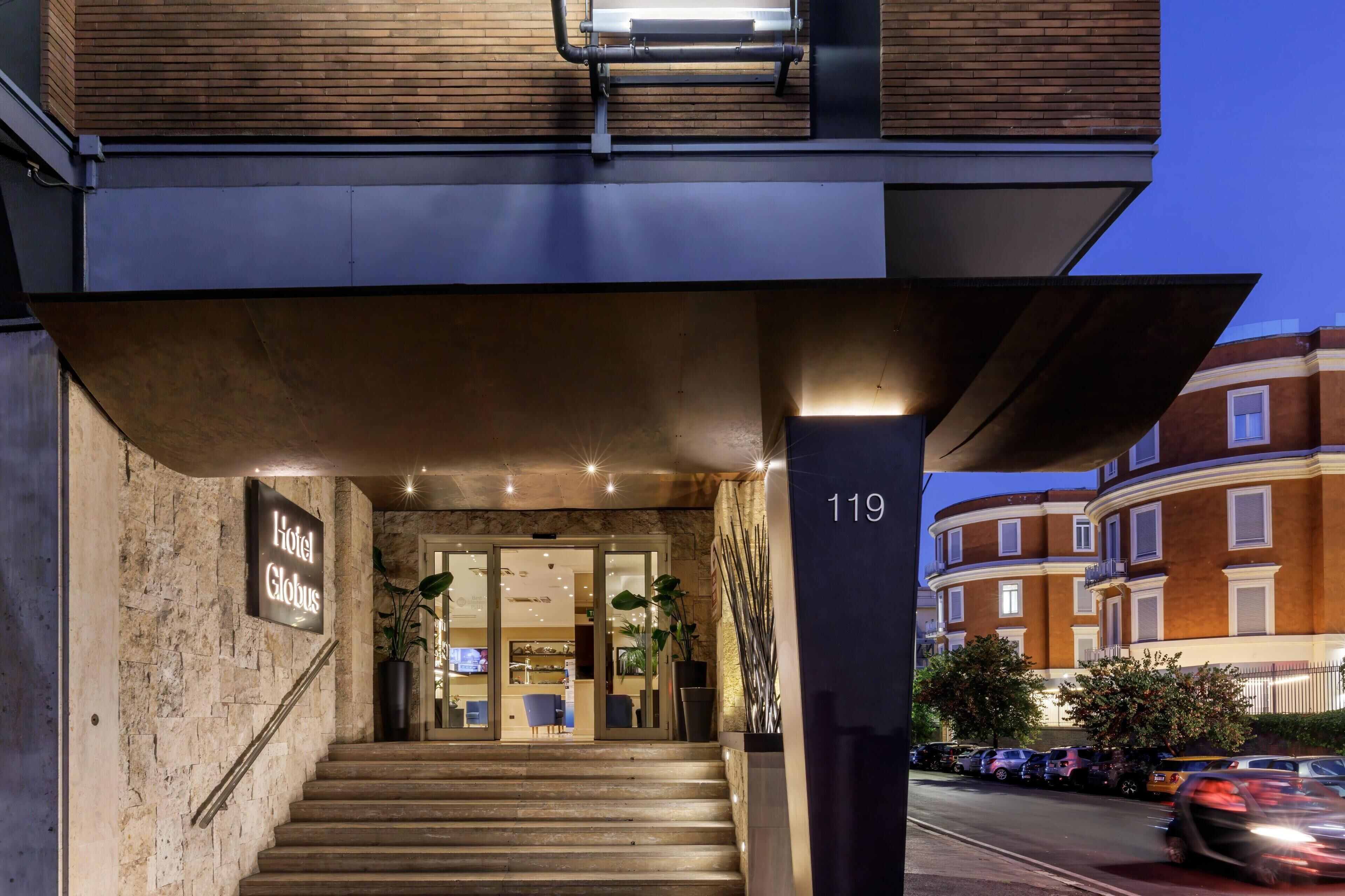 En hotellentrén med en trappa som leder upp till dörrarna, en skylt som visar hotellets namn och ett nummer ovanför entrén.
