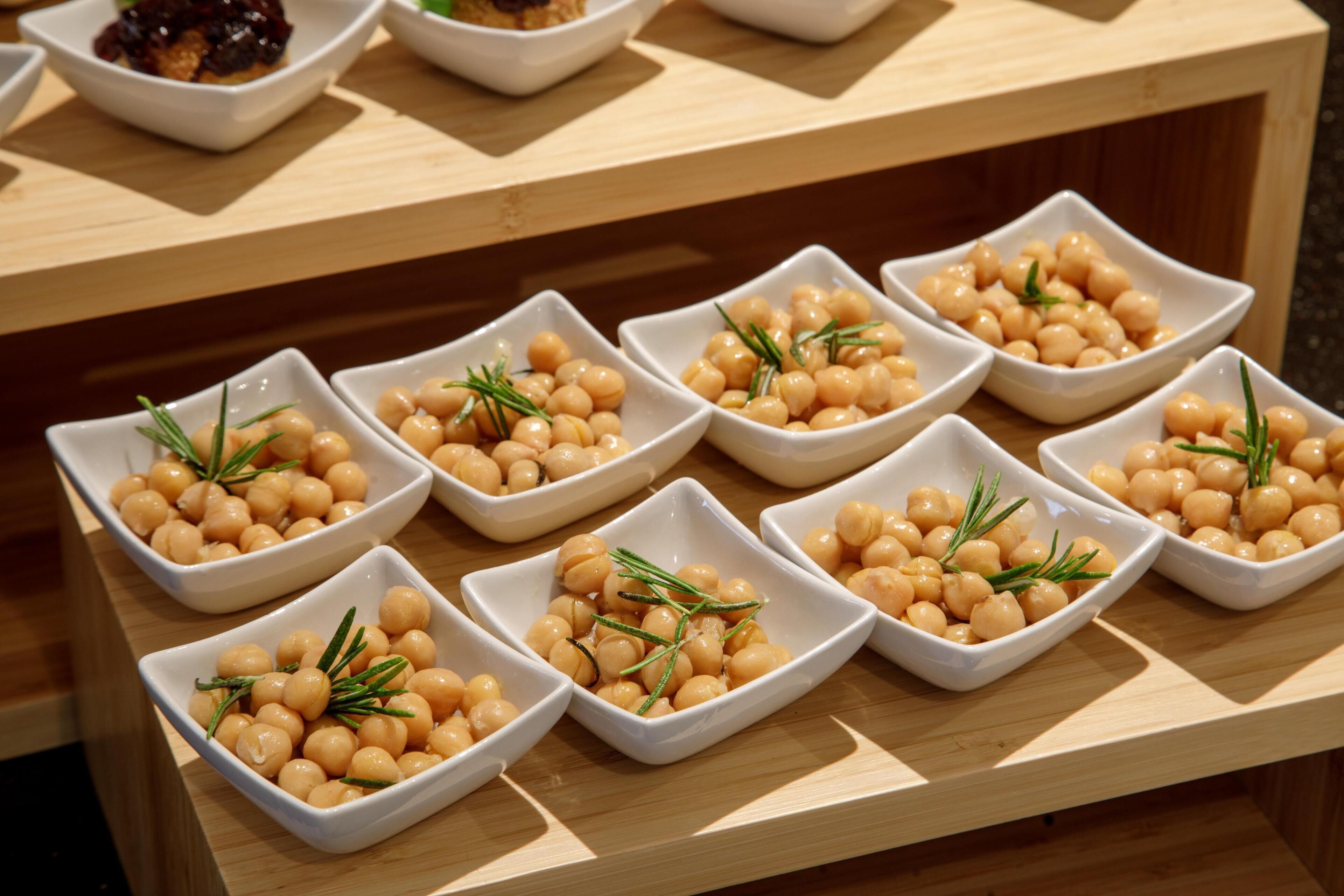 A table with multiple square white dishes containing chickpeas garnished with rosemary.