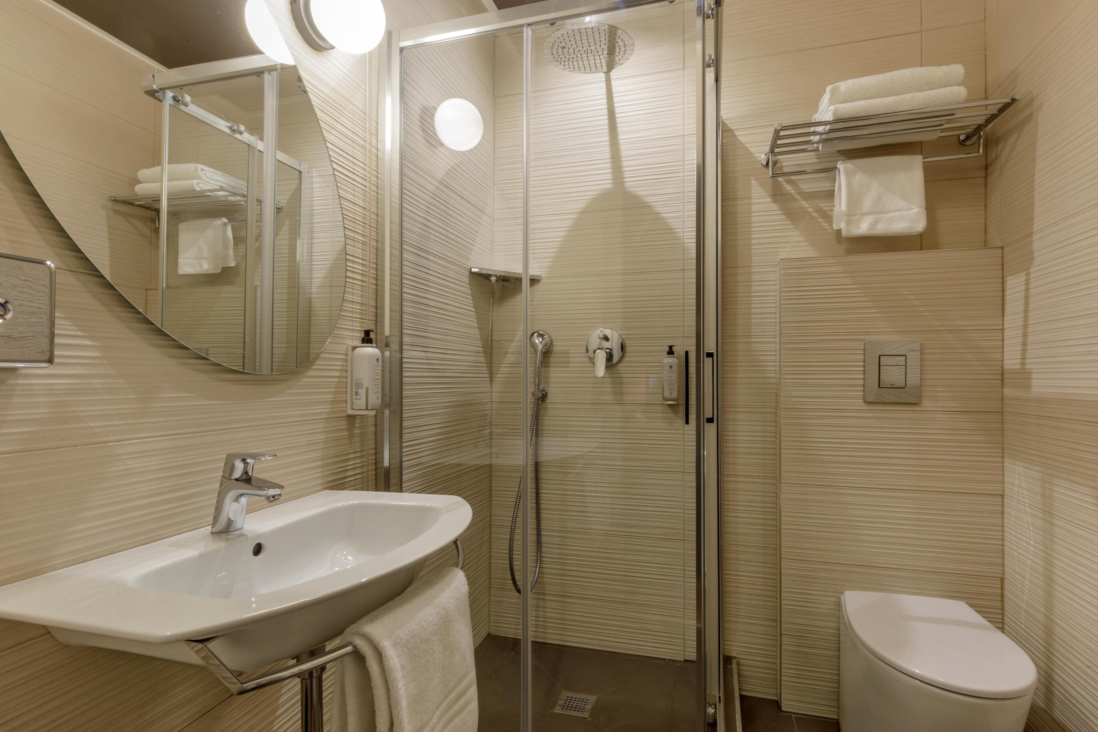 Ein modernes Badezimmer mit einer gläsernen Duschkabine, einem Waschbecken mit Spiegel und einer Toilette.