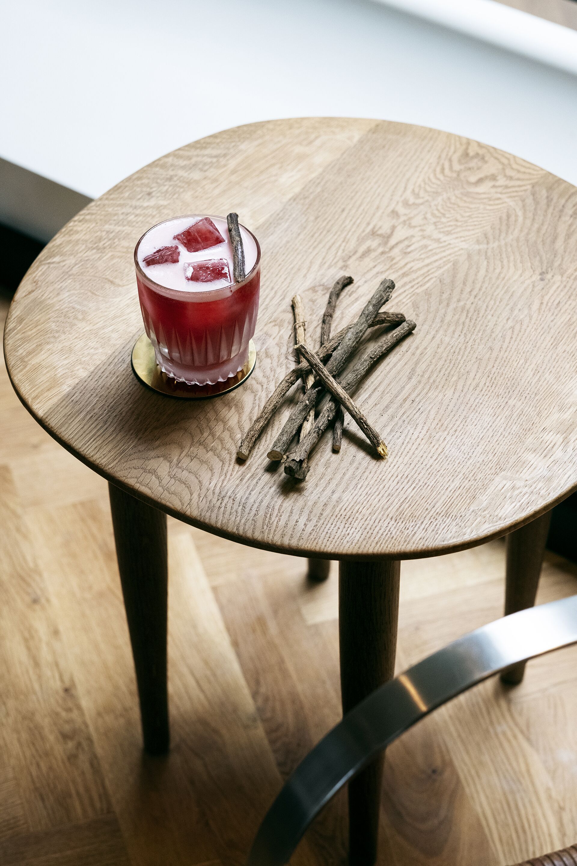 A round wooden table with a glass of red drink and cinnamon sticks on it.