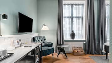 Un soggiorno moderno con TV a schermo piatto, una poltrona in velluto blu, un piccolo tavolino rotondo, una lampada e vista sulla città attraverso ampie finestre con tende grigie.