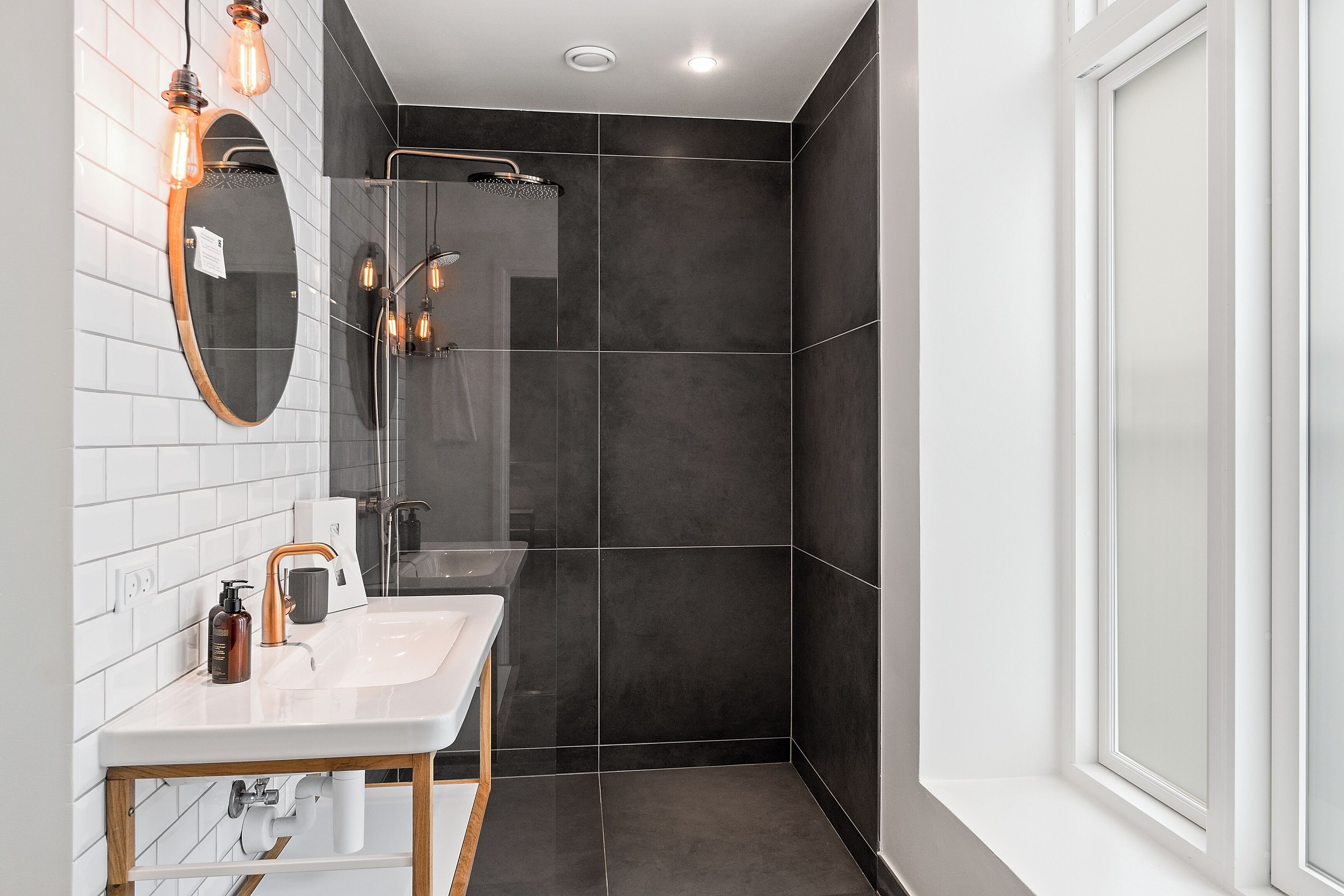 A modern bathroom with a white sink, mirror, and dark tiled shower area.