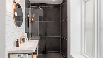 A modern bathroom with a white sink, mirror, and dark tiled shower area.