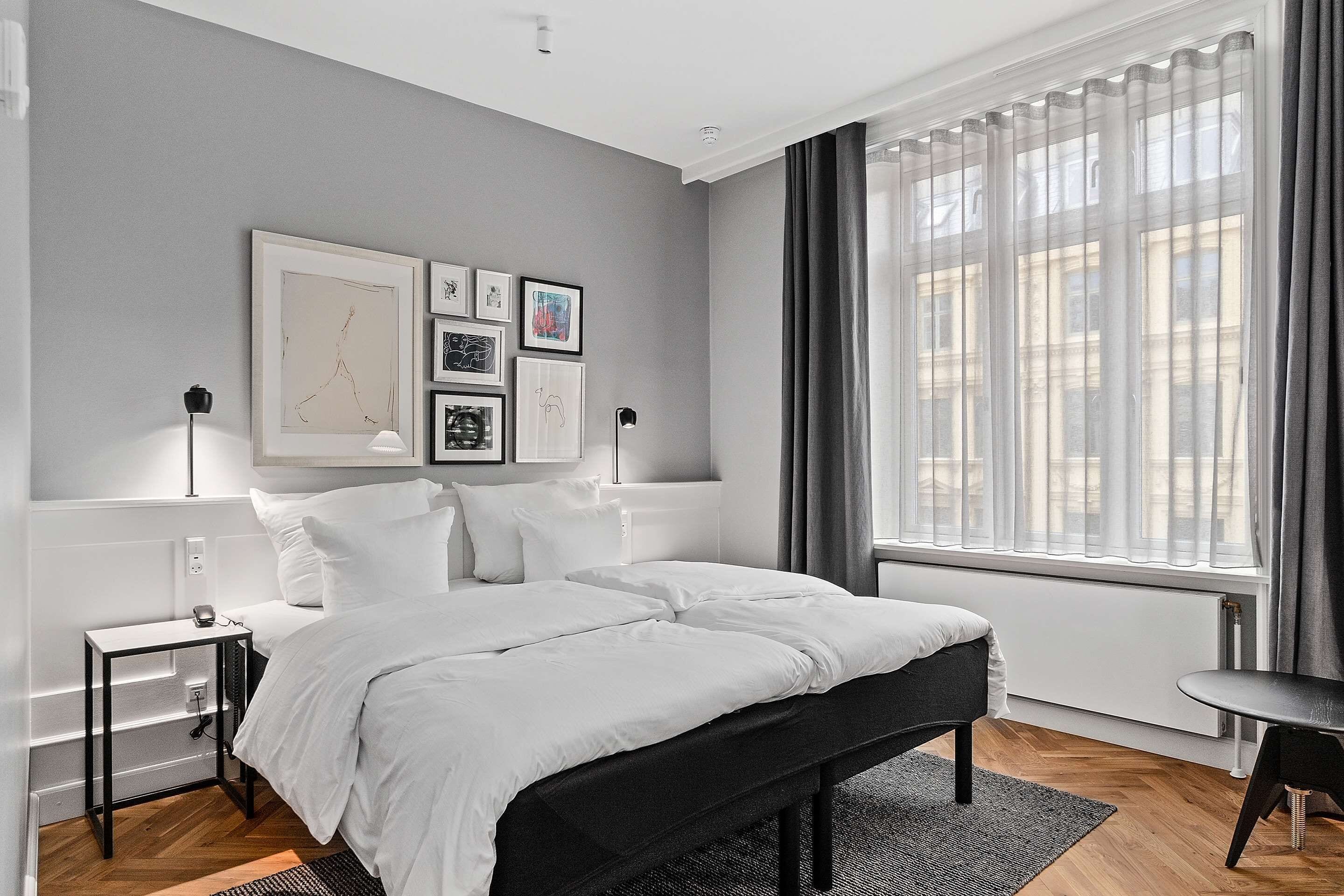 A modern bedroom with a large bed, bedside tables, a bench, and a window with curtains.