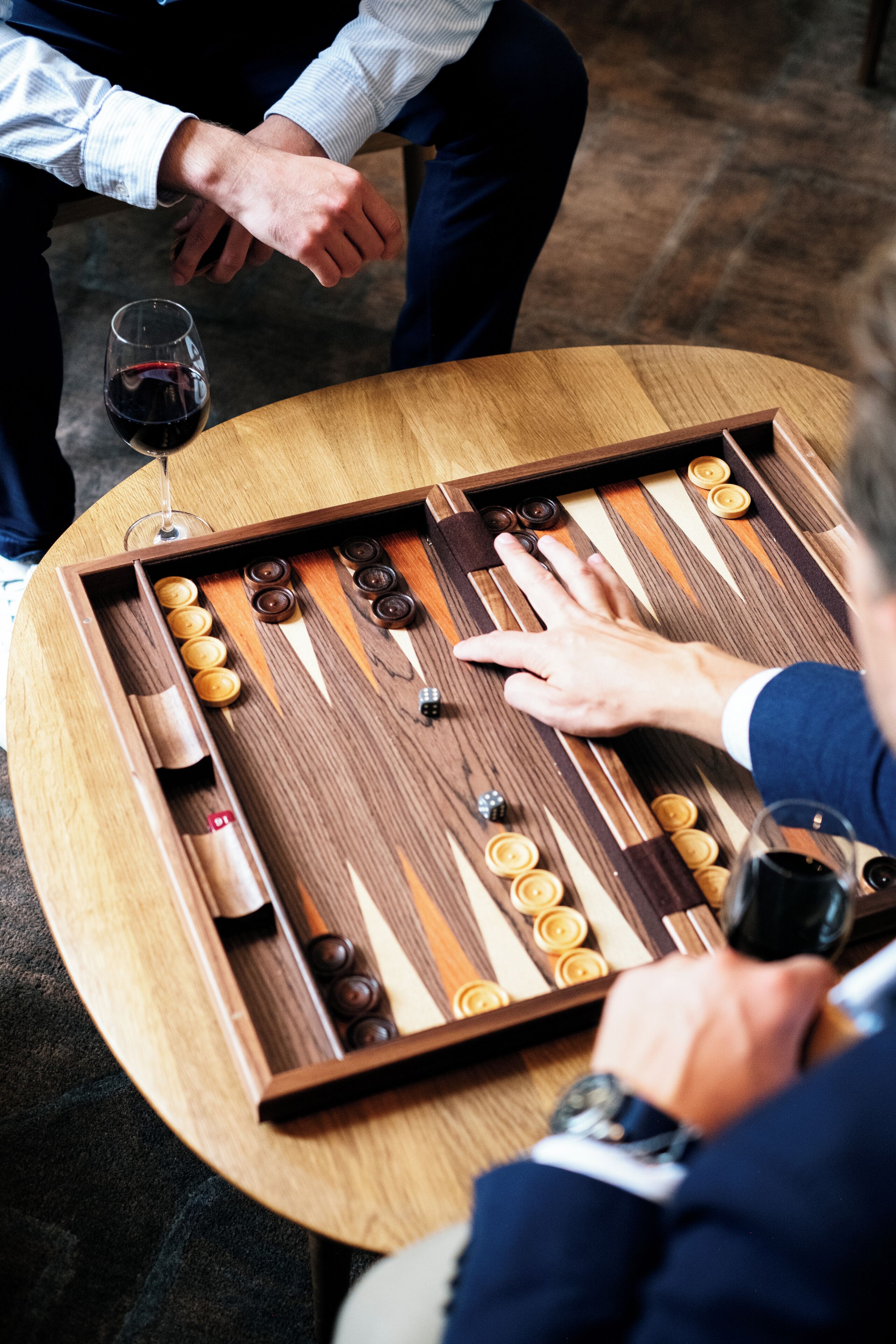 A wooden board game with pieces and a glass of red wine on a round table.