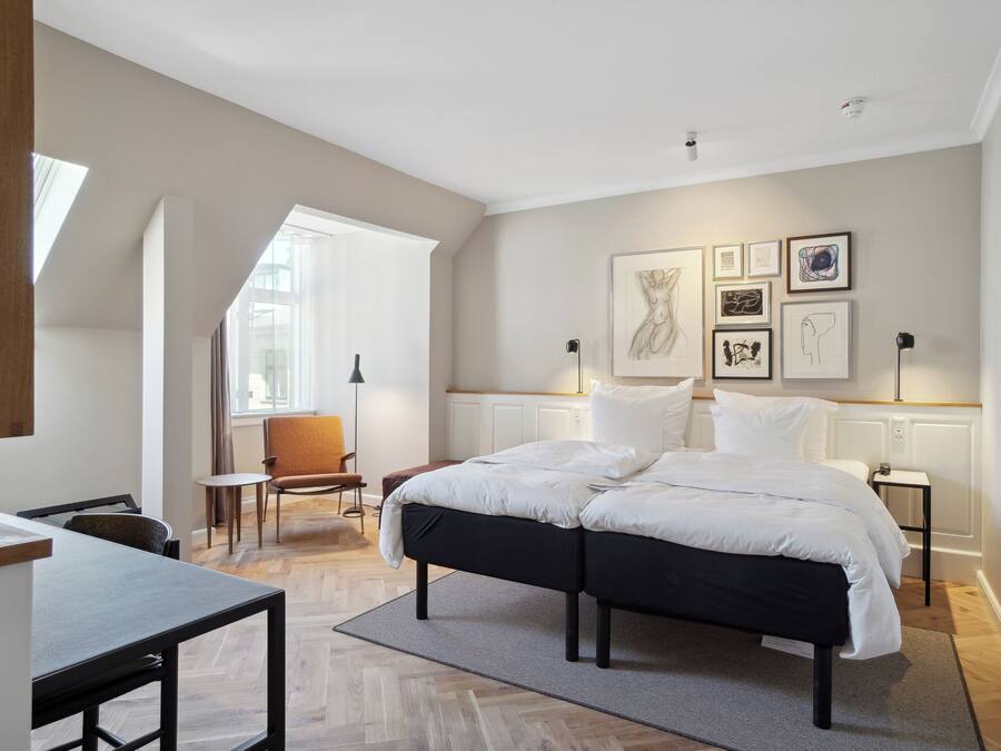 Un dormitorio con cama, mesitas de noche, una silla, un escritorio y obras de arte en la pared.