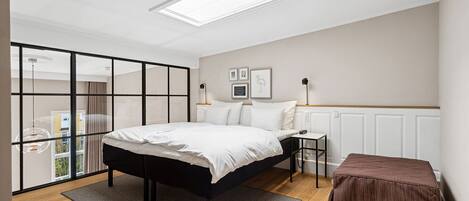 A modern bedroom with a bed, bedside table, and a view through a glass partition.
