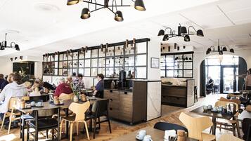 Un café moderno con mesas y sillas de madera, una barra central y lámparas colgantes.