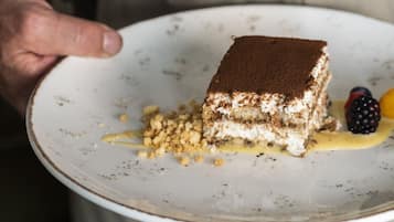 Una persona sosteniendo un plato con una porción de tiramisú y frutos rojos.