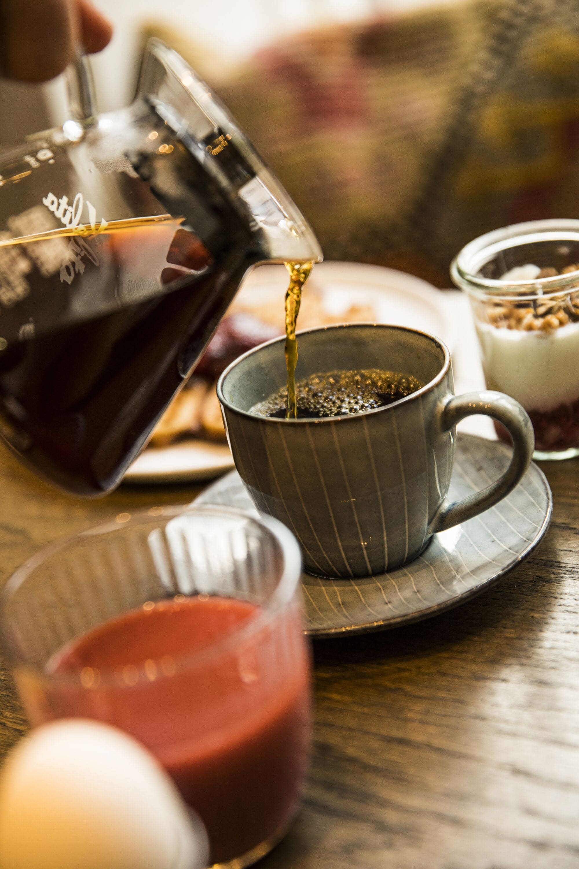 En kopp kaffe hälls upp i en mugg som står på ett bord.