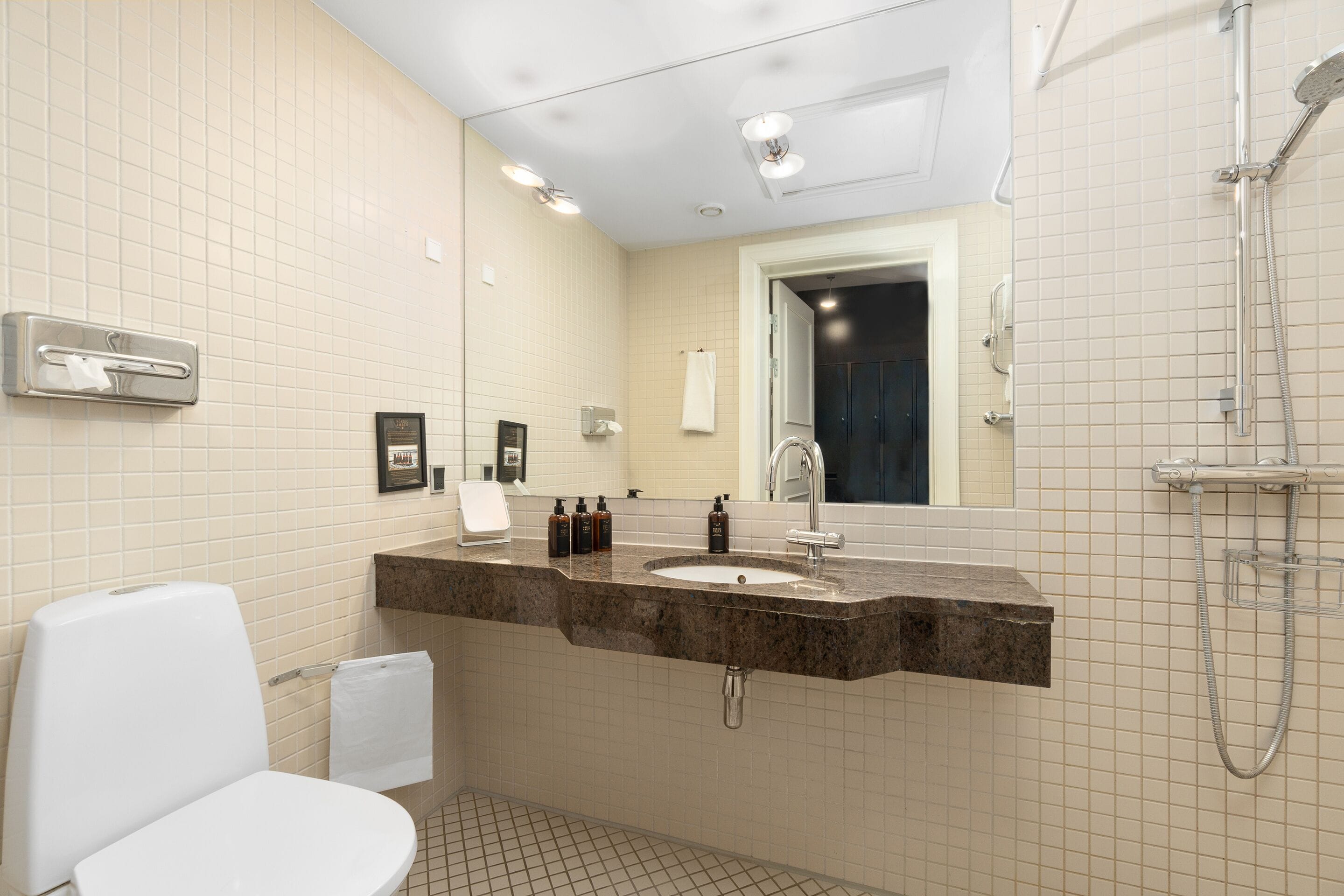 Un baño con inodoro blanco, lavabo con espejo y zona de ducha.