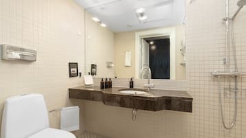 Un baño con inodoro blanco, lavabo con espejo y zona de ducha.
