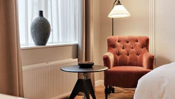 Ein Zimmer mit Fenster, Heizkörper, rundem Tisch mit Schale, Ohrensessel und Stehlampe.