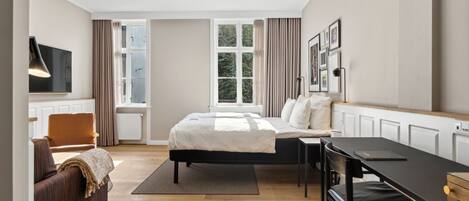 A modern hotel room with a bed, a desk, a chair, and a TV.
