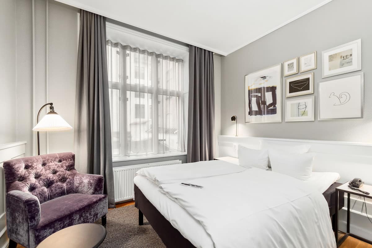 A hotel room with a bed, a chair, a desk, and a window with curtains.