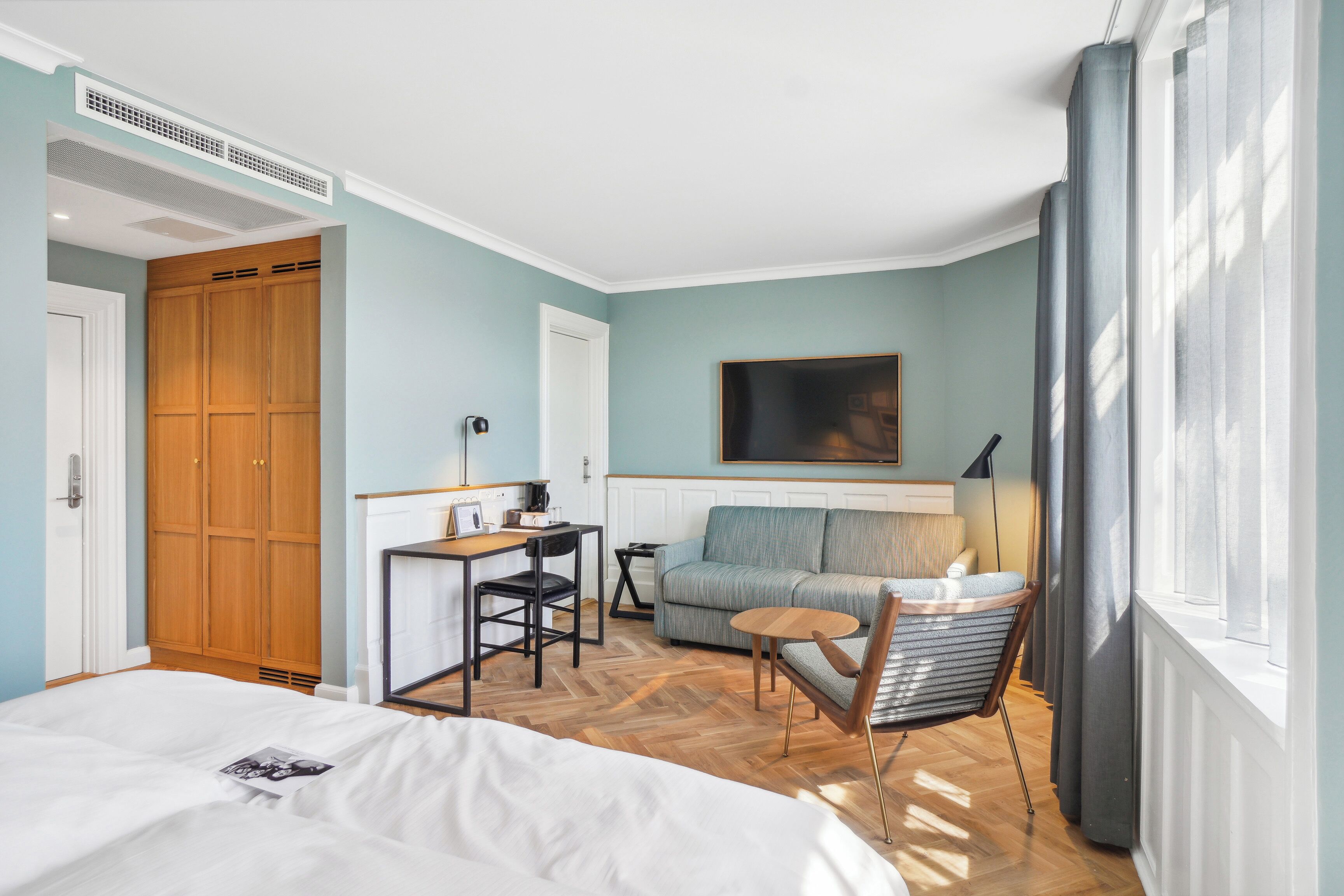 Une chambre d’hôtel avec un lit, un bureau et une chaise, un canapé et une fenêtre avec des rideaux.