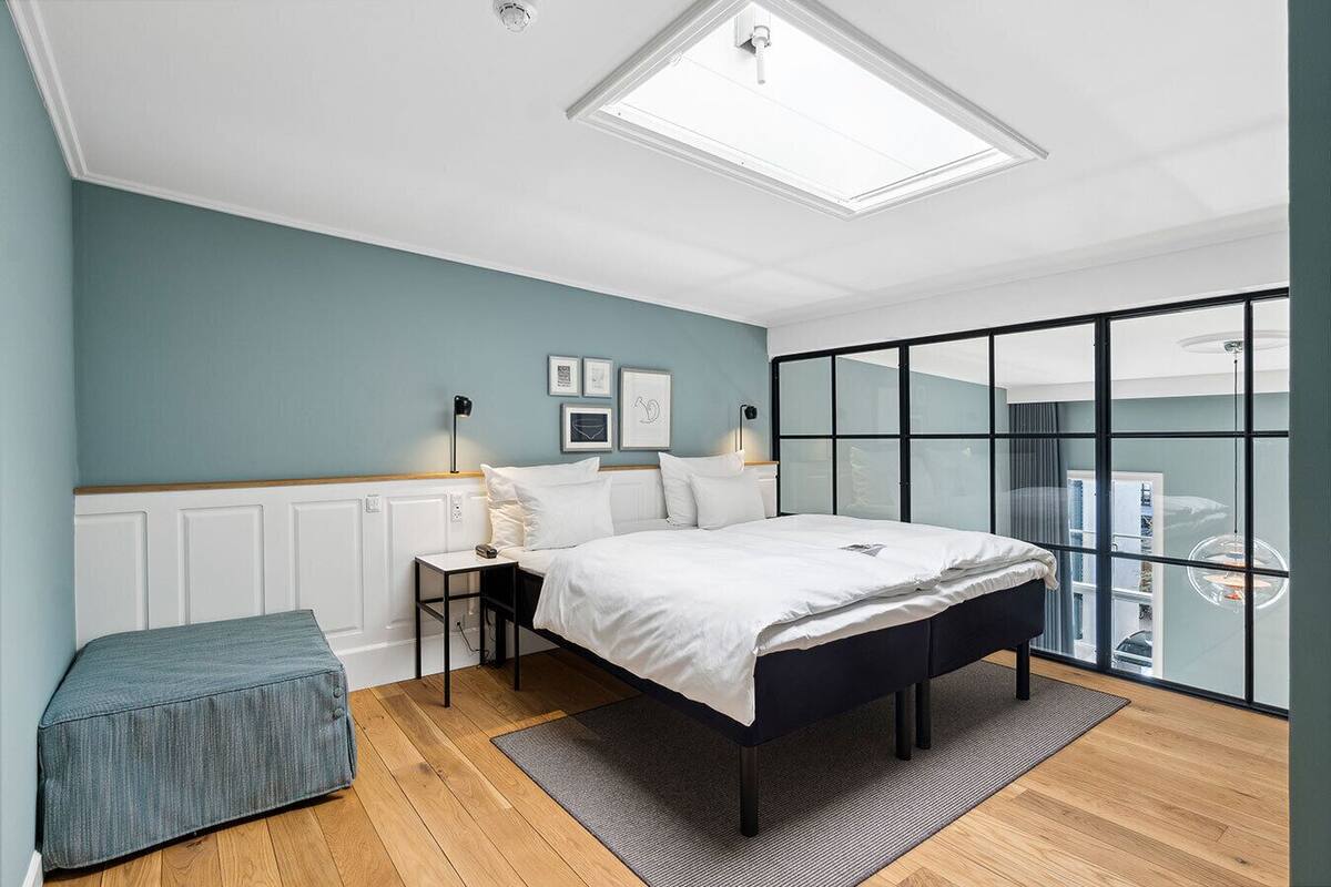 A modern bedroom with a skylight, a bed, a bedside table, a lamp, and a view through a glass door.