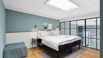 Un dormitorio moderno con tragaluz, cama, mesita de noche, lámpara y vistas a través de un ventanal.