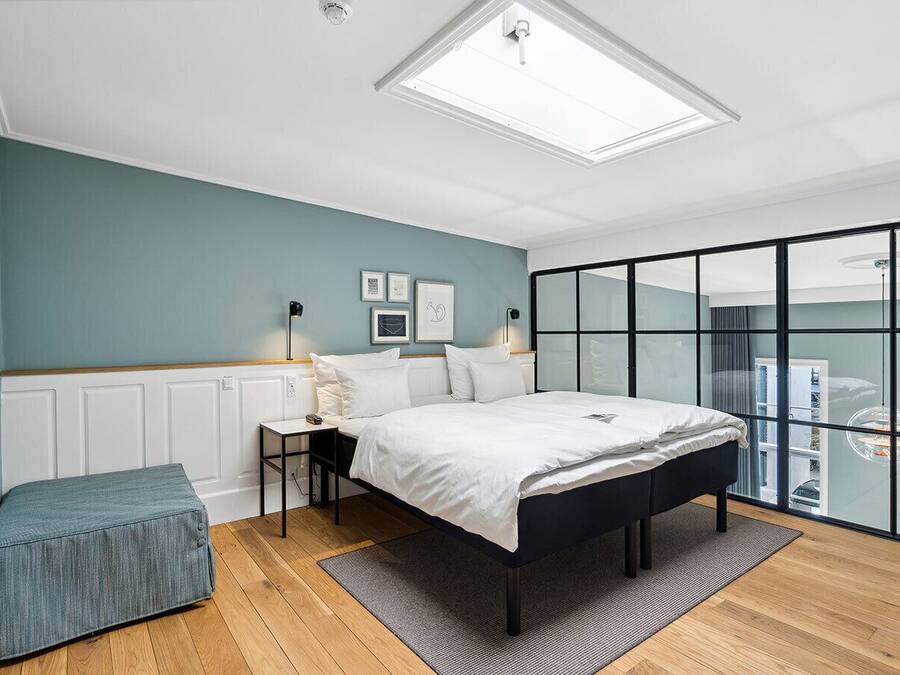 Une chambre à coucher moderne avec une lucarne, un lit, une table de chevet, une lampe et une vue à travers une porte vitrée.