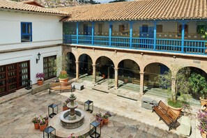 A courtyard with a fountain, benches, potted plants, and a balcony with blue railings.