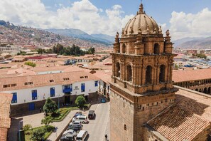A historic building with a prominent dome and bell tower, surrounded by a cityscape with red-tiled roofs and a hilly backdrop.