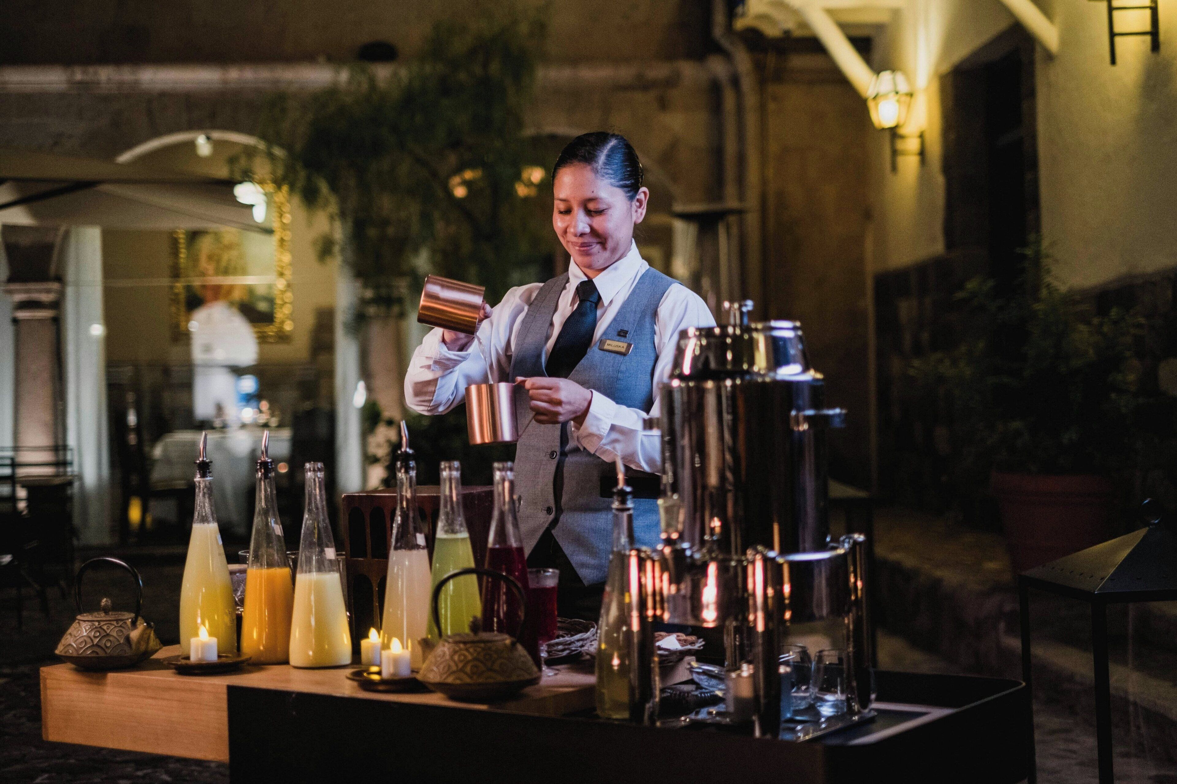 Zona de bar con un cantinero preparando bebidas, varios botellas y copas, y una vela sobre la barra.