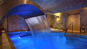 Un bassin de spa agrémenté d’une cascade, doté de murs en pierre et d’un espace détente avec des serviettes à disposition.