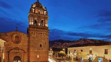 Um edifício histórico com uma torre imponente e entrada em arco, rodeado por uma rua de calçada e edifícios residenciais.