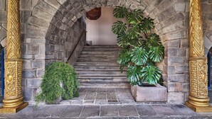 Un escalier en pierre, agrémenté d’une arche décorative et flanqué de colonnes dorées richement ornées, mène à un niveau supérieur.