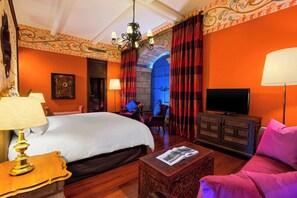 A hotel room with a large bed, a TV, a wooden coffee table, and a chair.