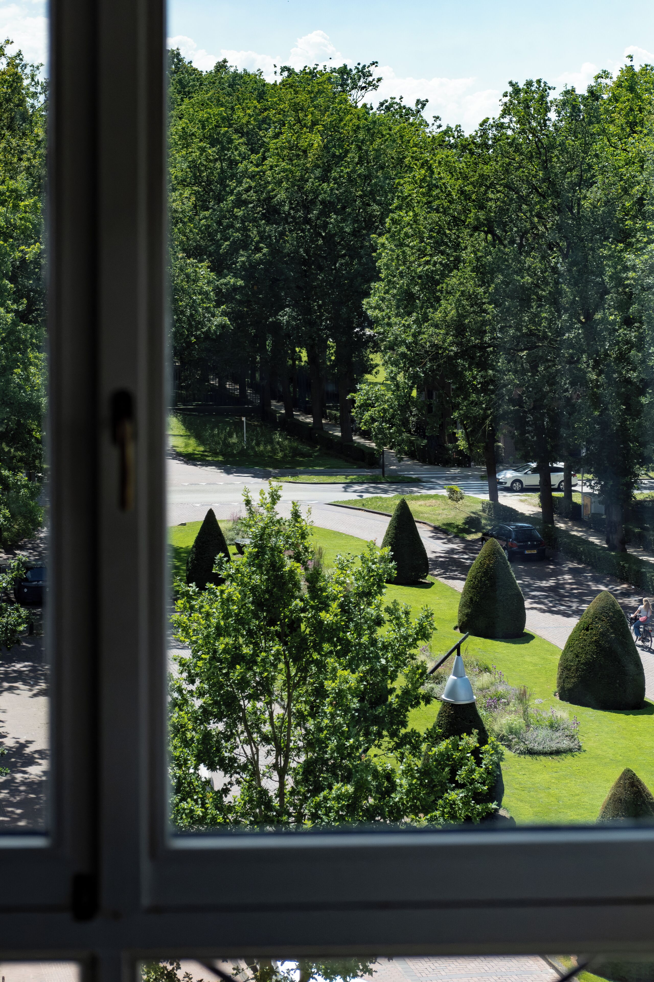 Vista a través de una ventana de un jardín cuidado, con setos podados y un camino empedrado.