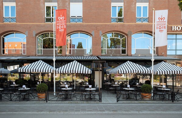 A hotel with outdoor seating and multiple flags. - Hotel Theater Figi (Zeist)