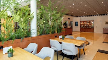 A hotel lobby with a reception desk, seating area, and indoor plants.